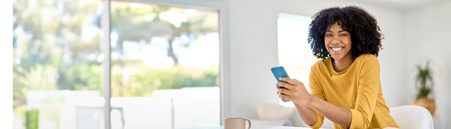 Jonge vrouw van kleur met een smartphone in haar hand kijkt lachend in de camera.