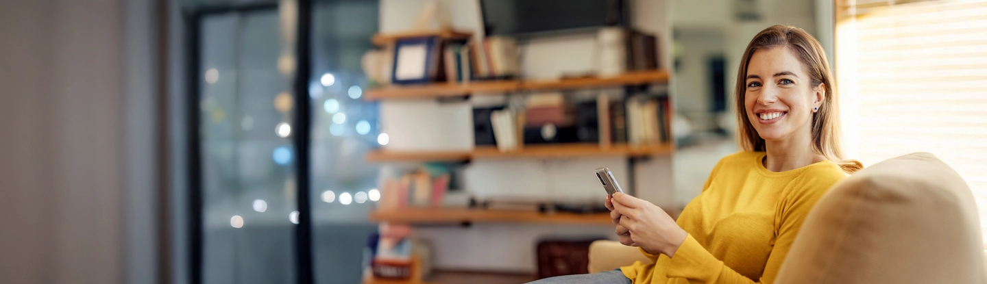 Jonge vrouw die op de bank zit met haar mobiel. En benieuwd is naar hoe Wizzer werkt.