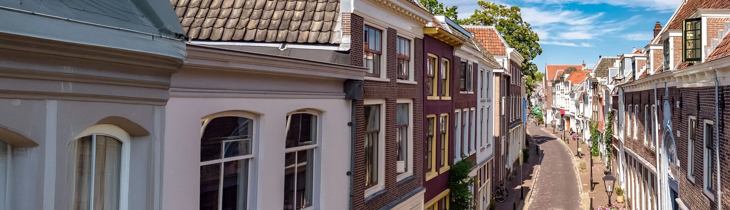 Straat in een Nederlands dorp, met mooie, historische huisjes, tegen een blauwe lucht met witte wolken.