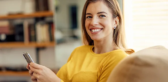 Jonge vrouw die op de bank zit met haar mobiel. En benieuwd is naar hoe Wizzer werkt.