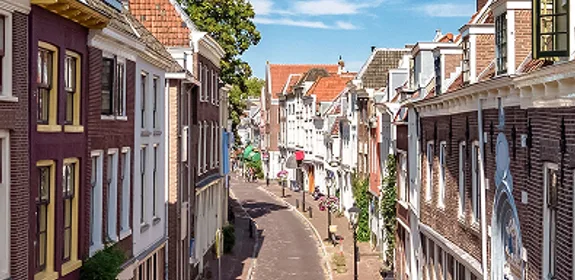 Straat in een Nederlands dorp, met mooie, historische huisjes, tegen een blauwe lucht met witte wolken.